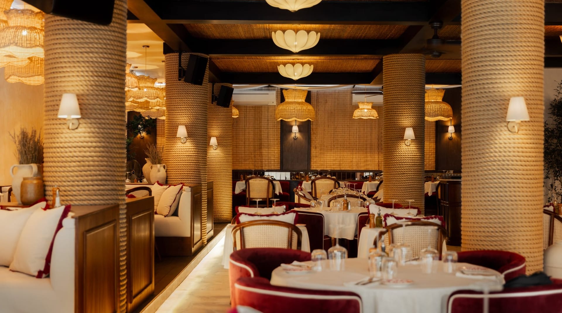 The dining room, scalloped lamps above tables laid with white linen and burgundy chairs