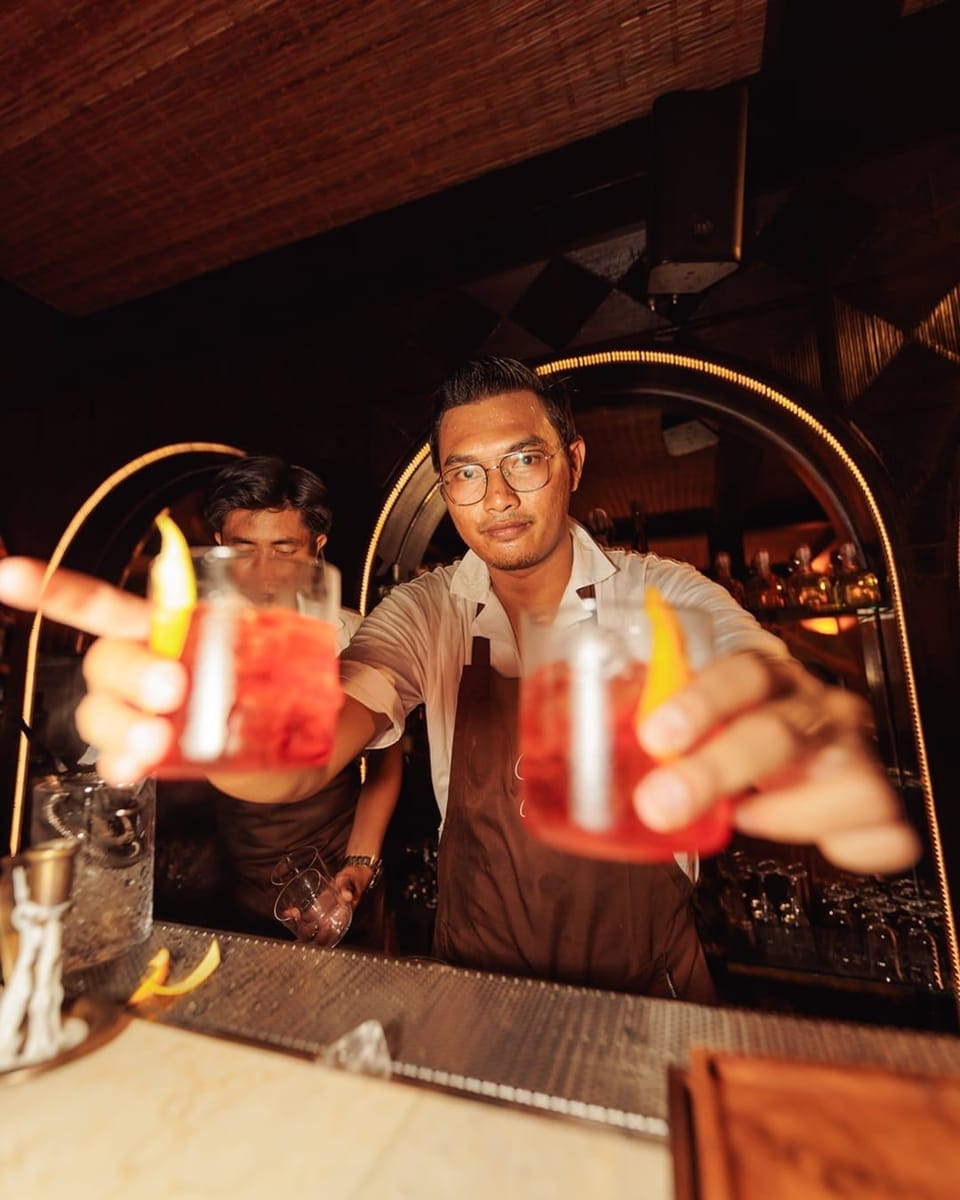 A bartender at Giselle holding two red cocktails