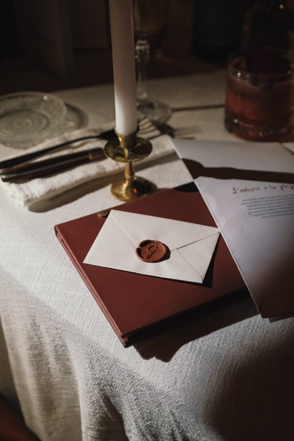 An envelope closed with a wax seal on a red book beside a candle