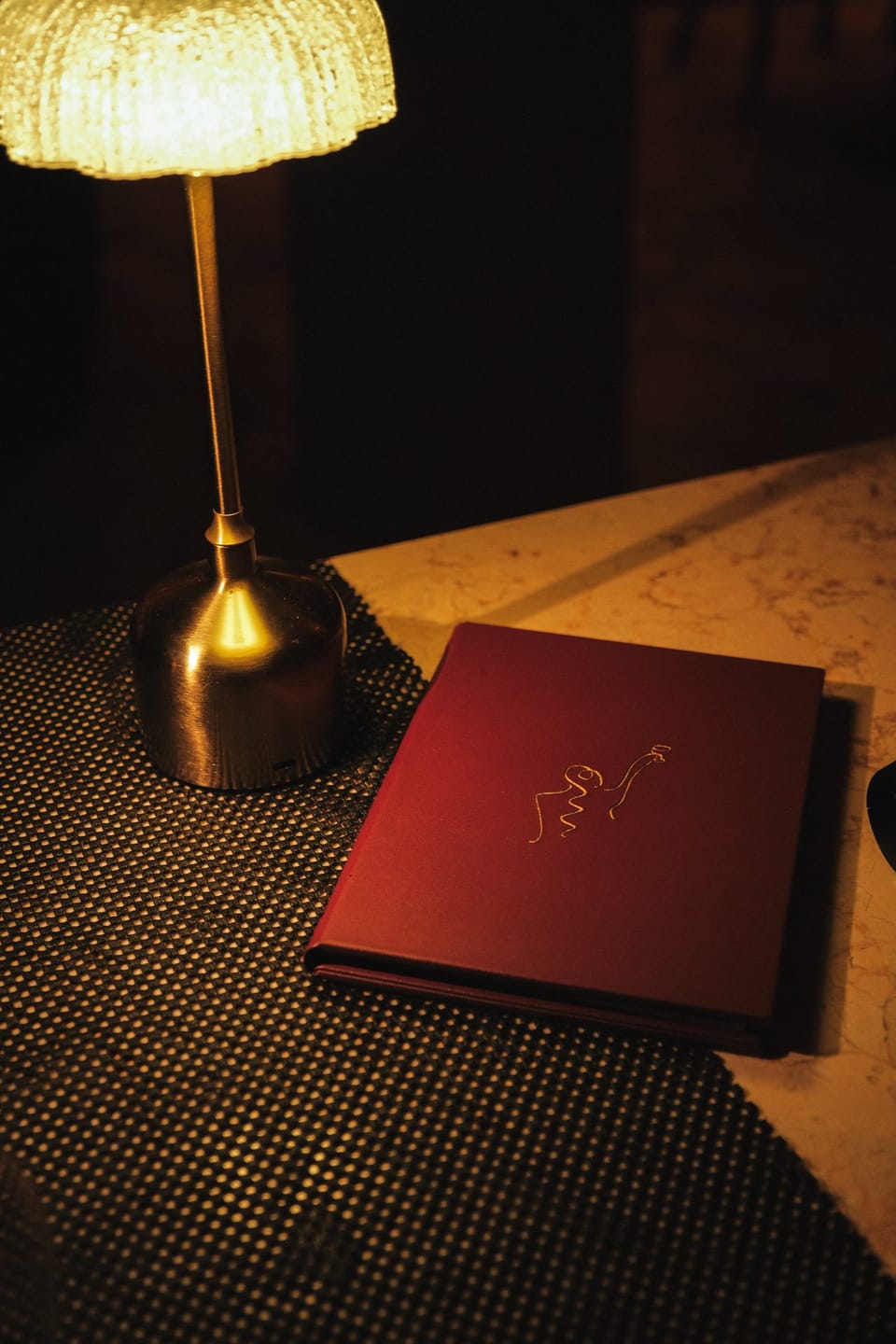 The burgundy Giselle menu book under a brass lamp