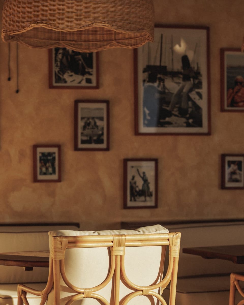 A wall of framed photographs above a rattan chair at Giselle