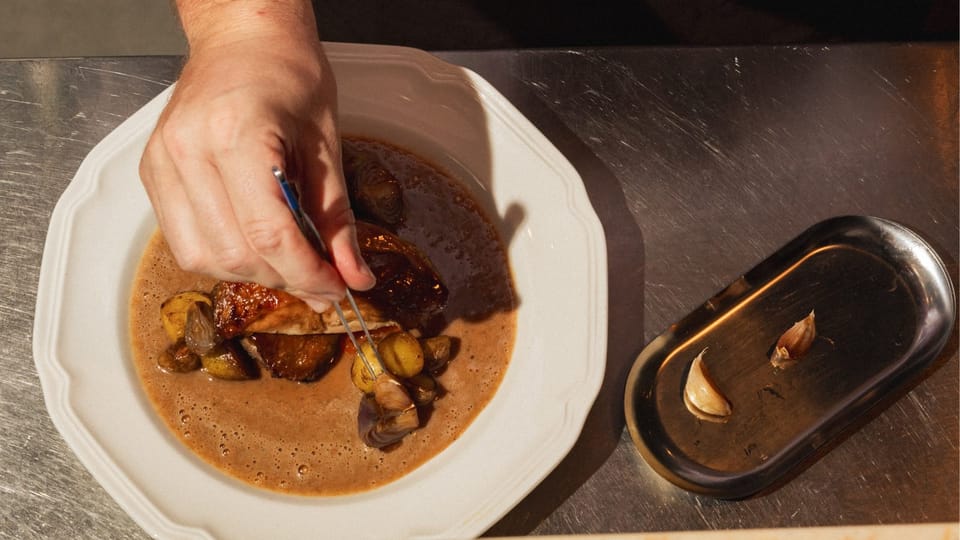 A hand plating a dish at the pass