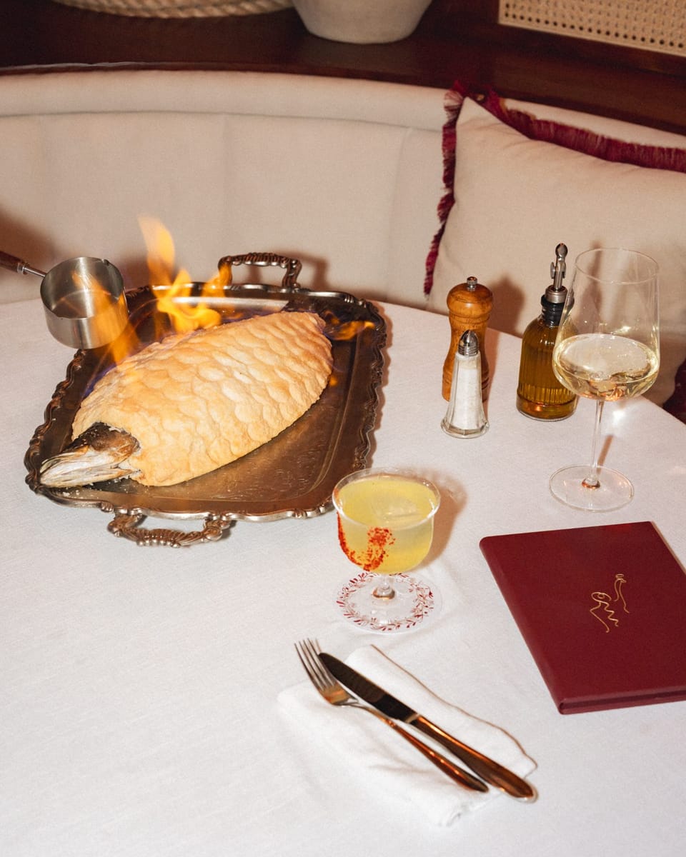 A whole fish in salt crust flambéed at the table, beside the red menu book