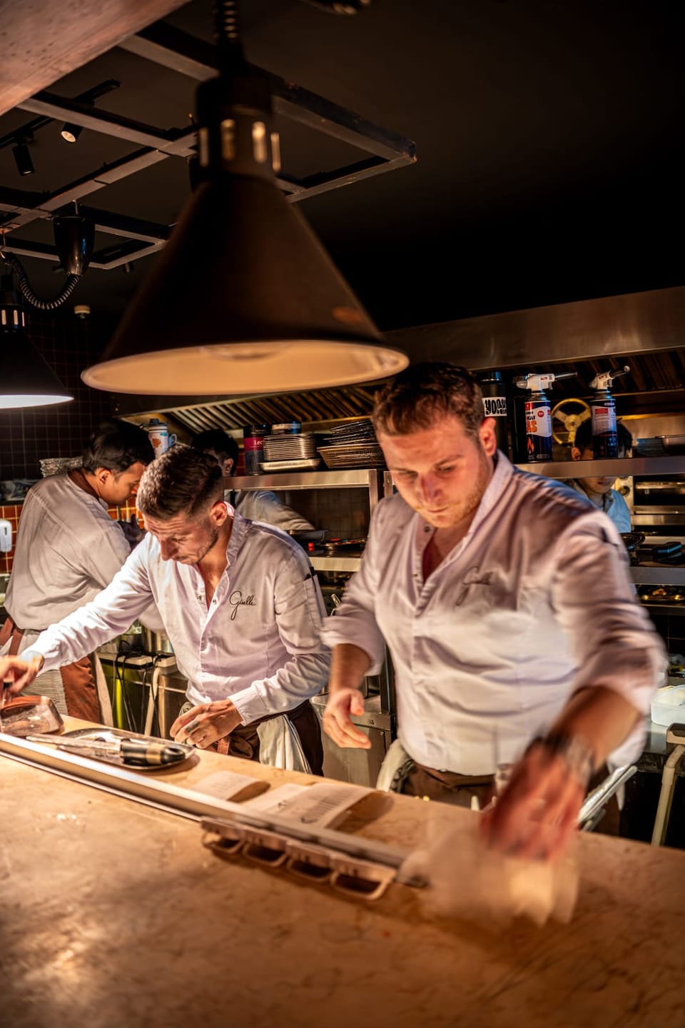 Two cooks working at the pass under the lamps
