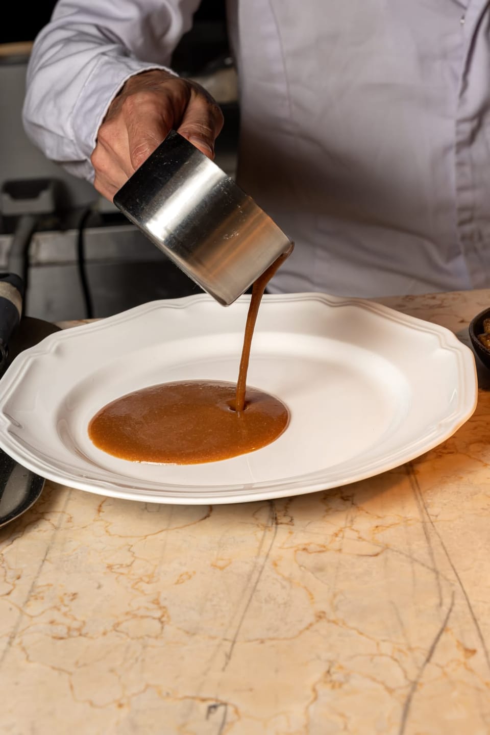 A sauce poured into a white plate on the marble pass