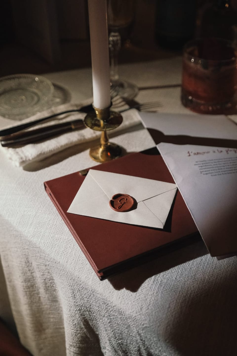 An envelope closed with a wax seal on a red book, on a table laid with linen
