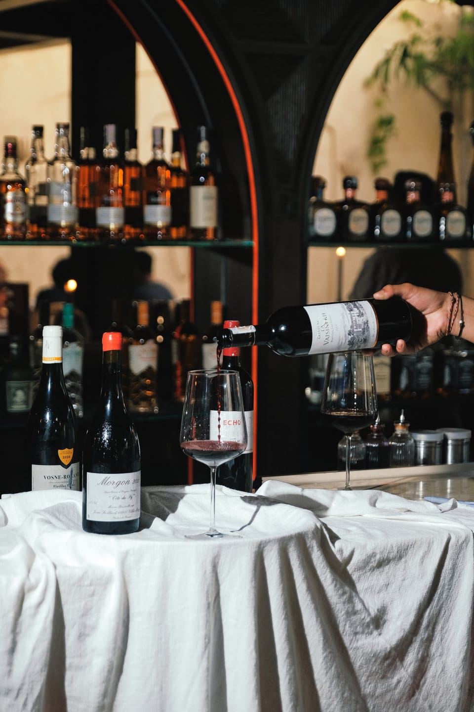 Red wine poured at the bar, bottles on the shelves behind